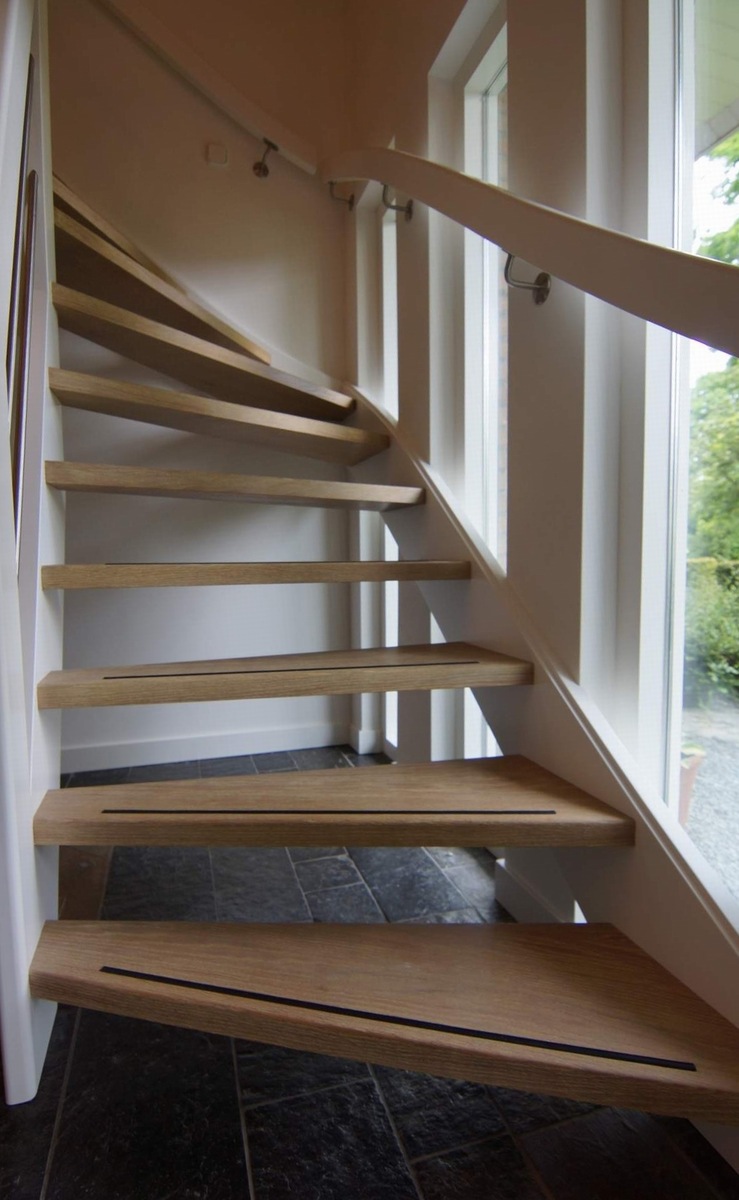 moderne trap,houten trap,Ulvenhout,Breda,Nederland,close-up van de eiken treden van deze open trap,voorzien van antislip, treden tussen de beuken trapwangen die we wit geschilderd hebben voorzien,zicht op de witte muurgreep aan de muurzijde
