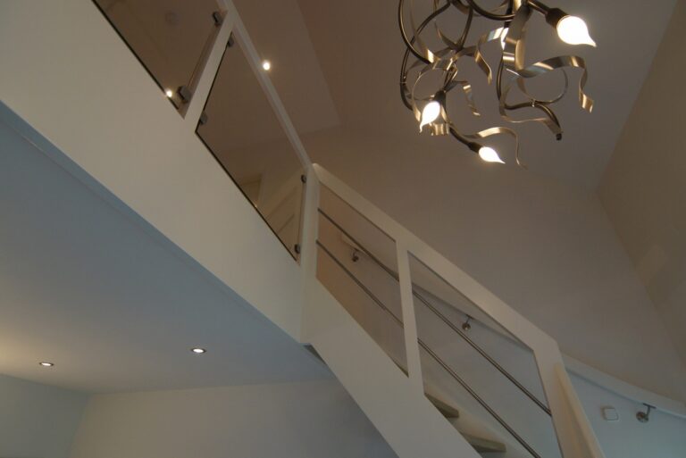 moderne trap,houten trap,Ulvenhout,Breda,Nederland,zicht op de RVS spijlen en de combinatie van wit geschilderd beukenhout met glas op de balustrade van de verdieping,overloop